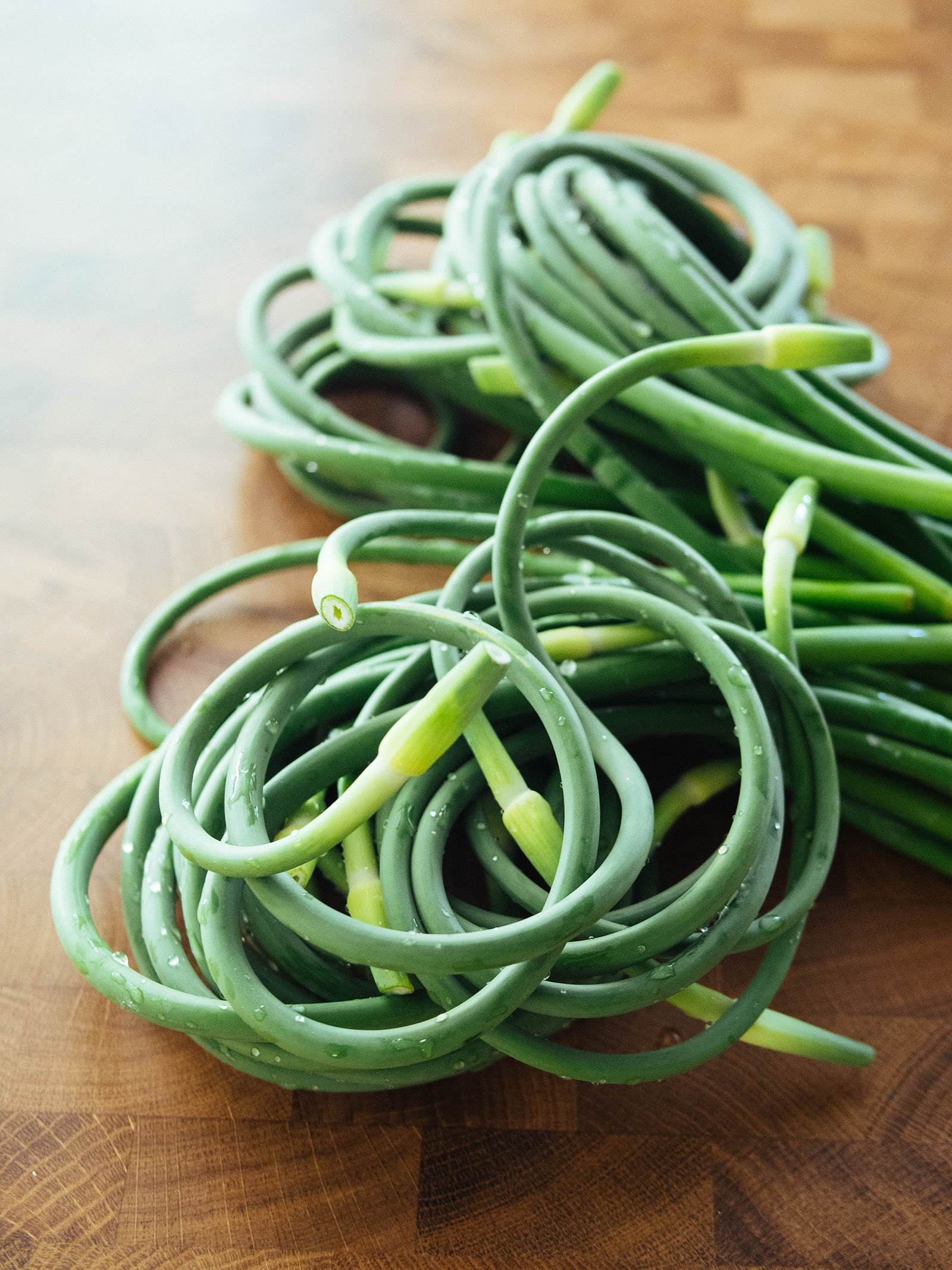 Two bundles of garlic scapes on a wooden kitchen counter